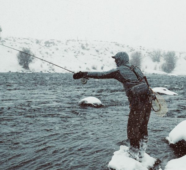 A man fly fishing in the snow in the Gallatin River, one of the best things to do in Big Sky Montana in winter or summer