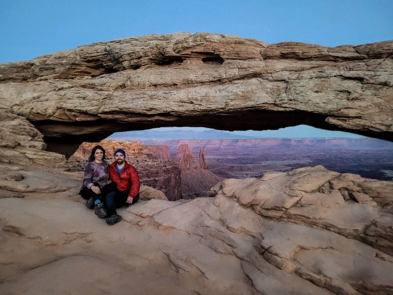 Two people sitting near Mesa Arch, one of the best hikes in Canyonlands