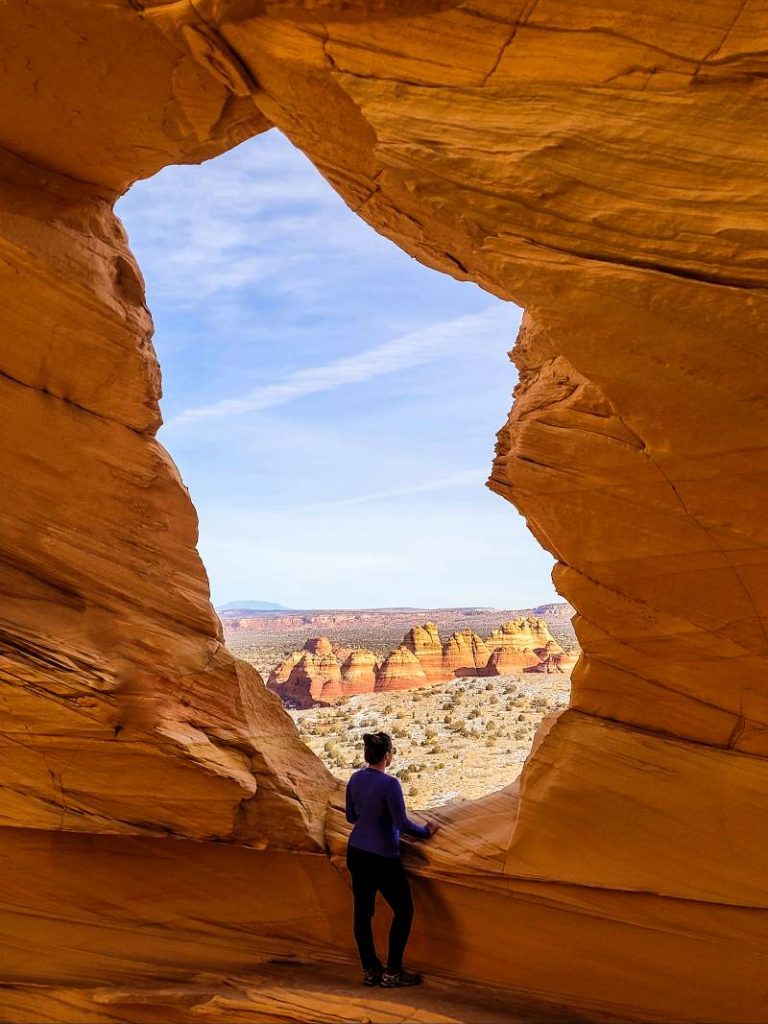 A woman looking through a natural window in a rock at The Wave Arizona