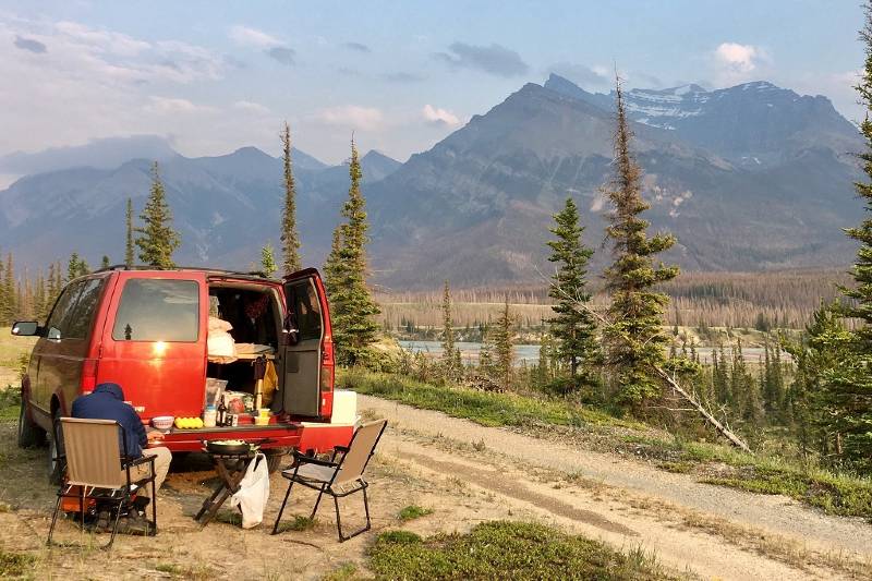 A man preparing a meal outside a campervan with mountains in the background