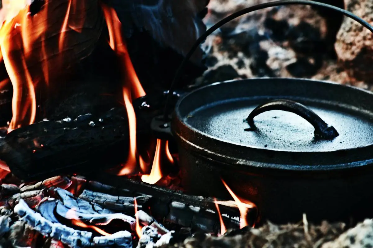 A close-up of a campfire with a cast iron Dutch oven nestled into the embers