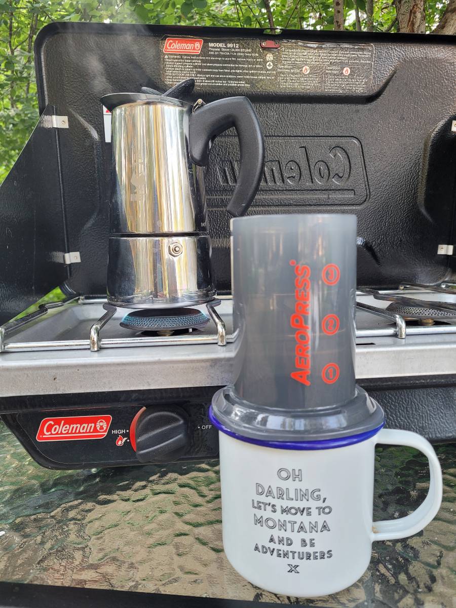 An Aeropress on a coffee mug and a Bialetti Moka Express on a Coleman camp stove, all important camping must haves