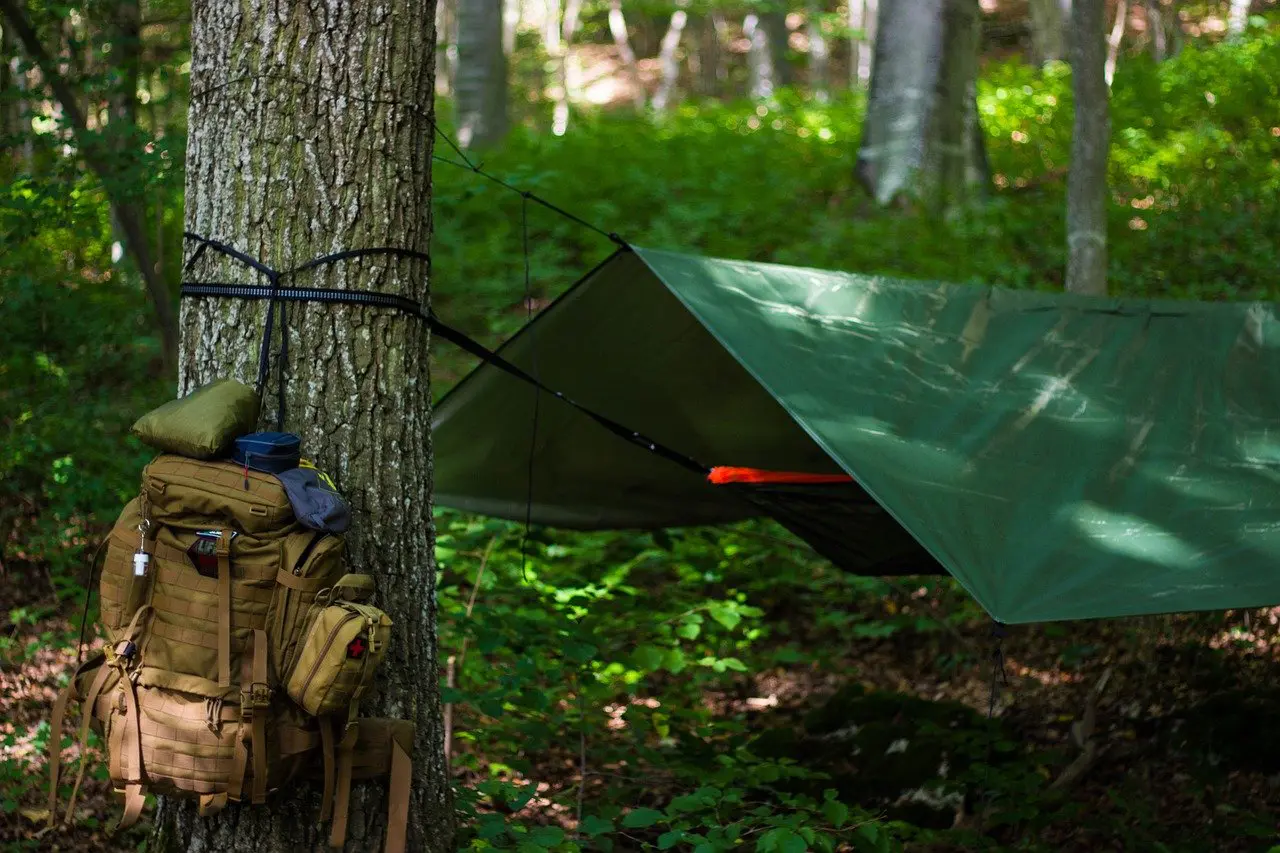 A backpack with gear tied to a tree and a strung-up hammock, one of the most versatile camping must haves