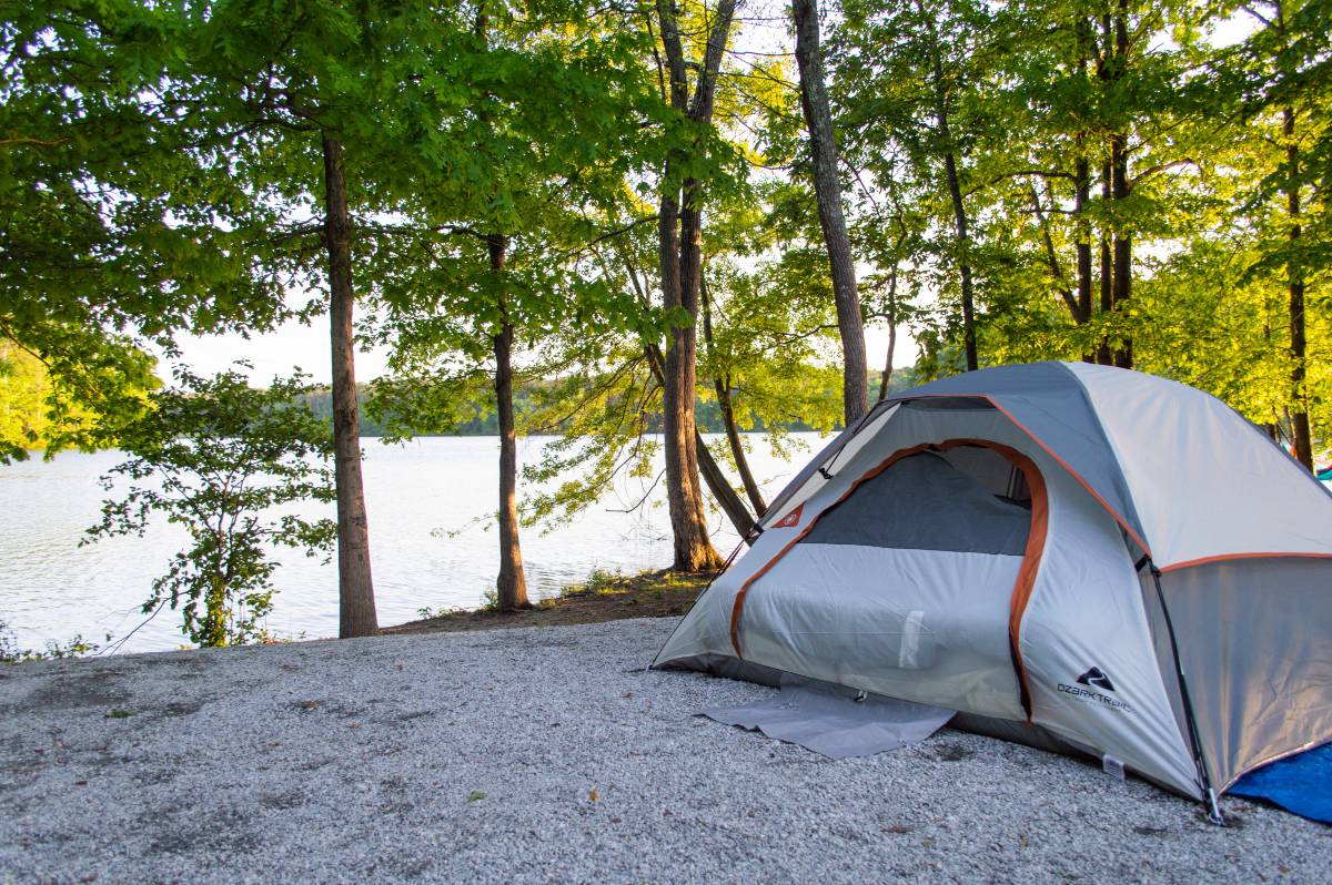 A gray tent pitched near a lake and trees