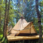 A tipi on a deck in the woods at Bodhi Farms, a resort for glamping in Montana near Yellowstone National Park