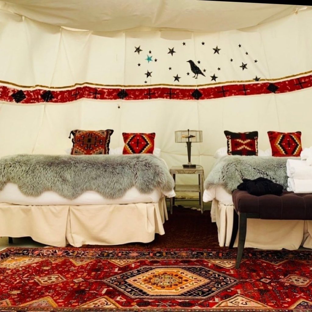 The interior of a tipi with two beds and luxe linens at Dreamcatcher Tipi Resort, one of the best options for glamping in Montana