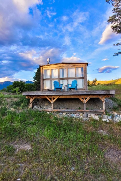 A cabin with two Adirondack chairs on the deck at Tobacco River Ranch, a resort for glamping in Montana