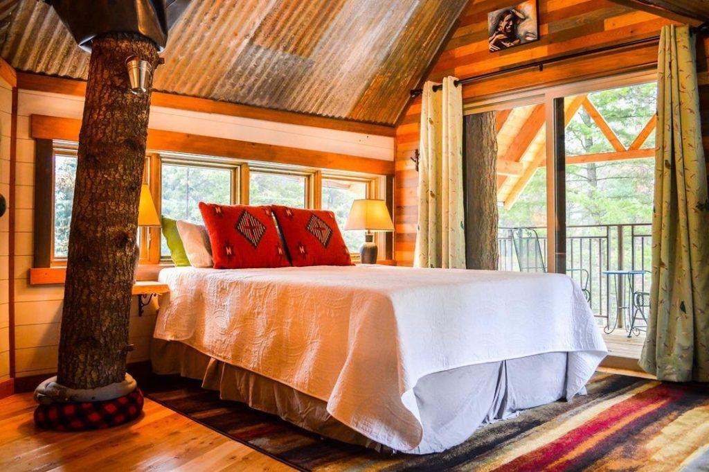 A bed surrounded by windows and doors at Montana Treehouse Resort, a property for glamping in Montana