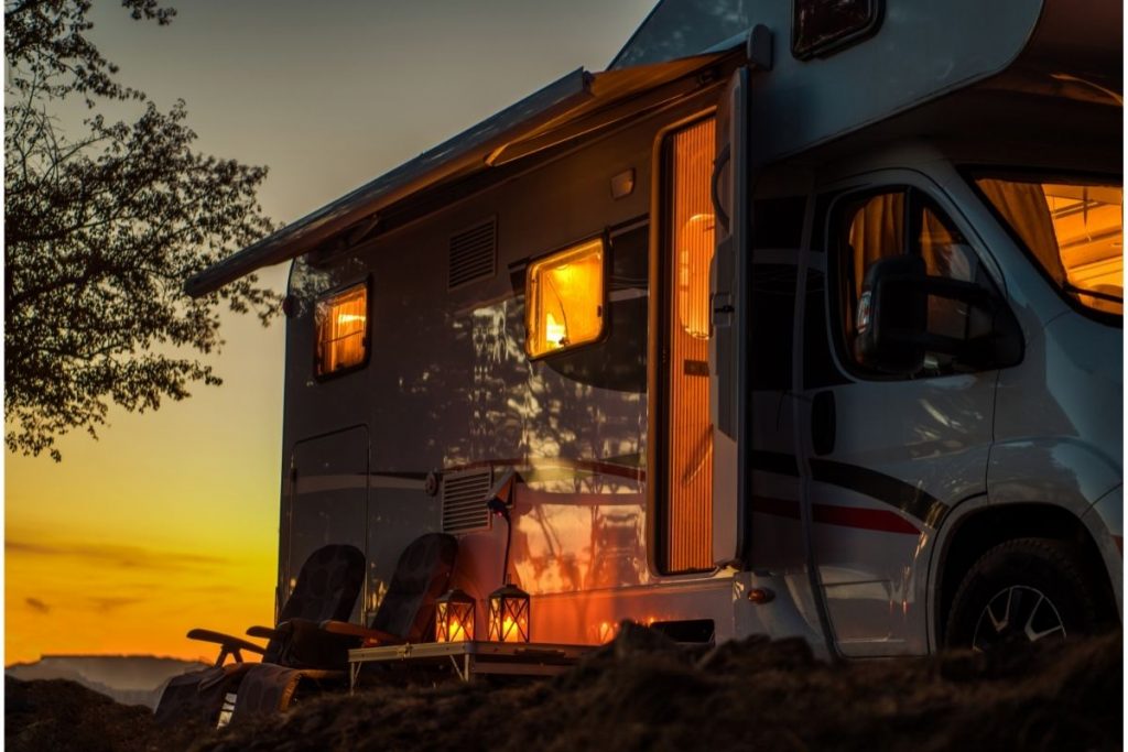 An RV at sunset with chairs set up out front, one of many campsites you may find by reading Harvest Hosts reviews