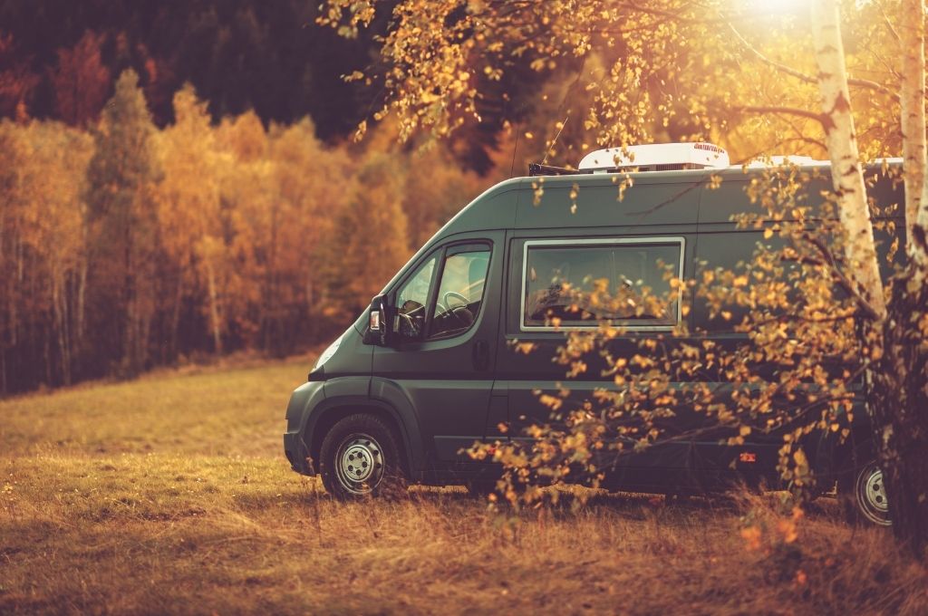 A campervan parked in a field surrounded by fall foliage at one of many scenic Harvest Host locations