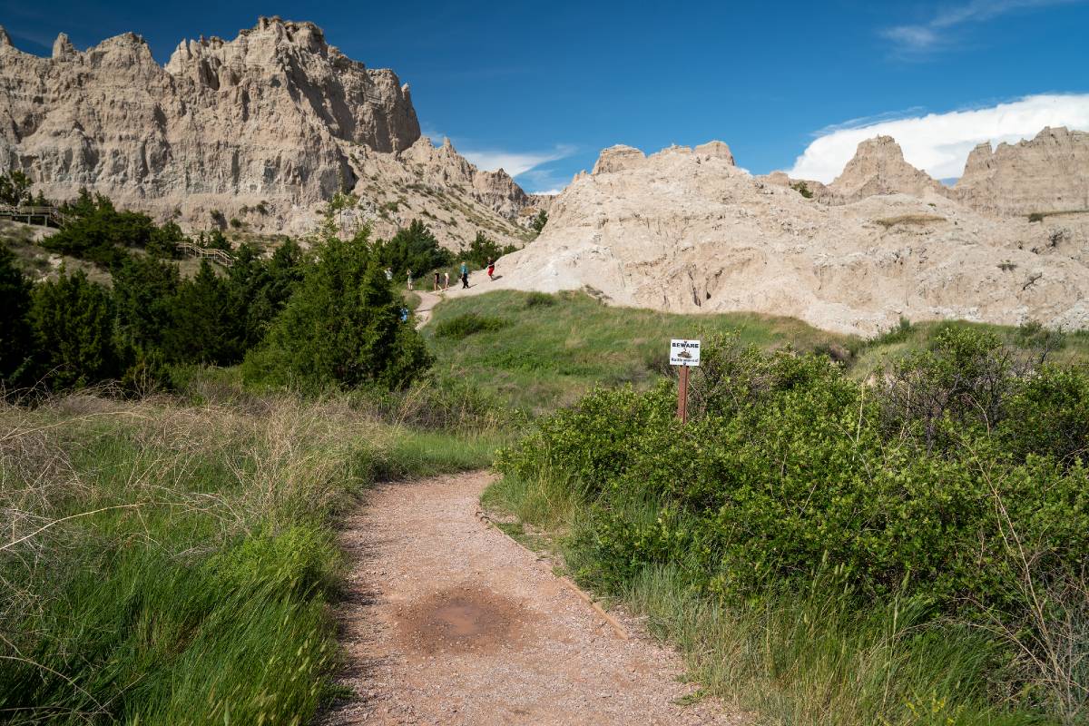 The start of a trail and hikers climbing a pass in the distance on the Cliff Shelf Nature Trail, one of the most underrated hikes in the Badlands