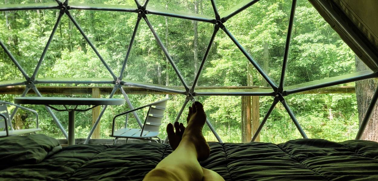 A person relaxing on a bed inside Treehouse Dome at Glamping Unplugged