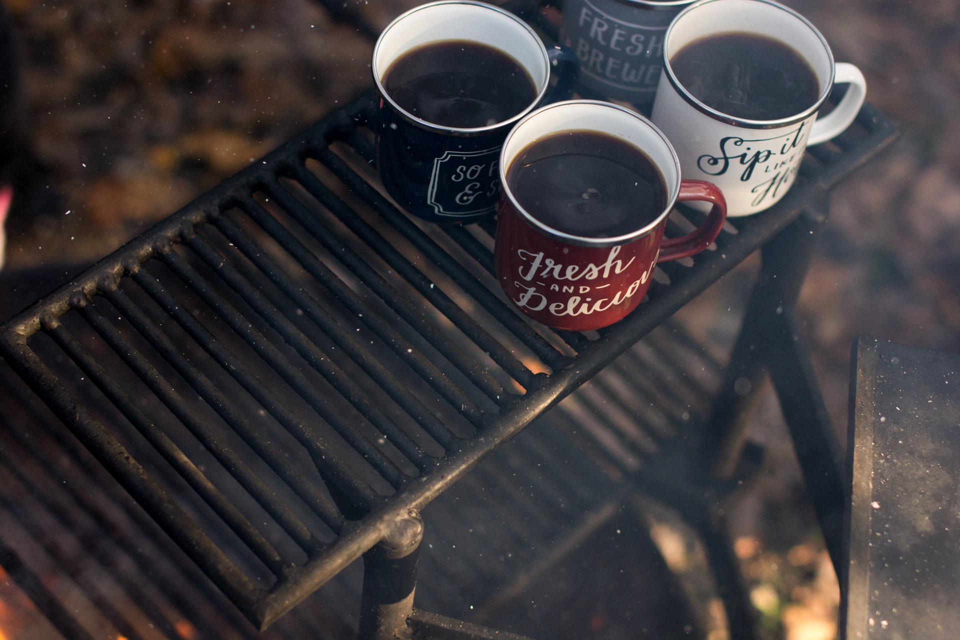 Four mugs of camp coffee sitting on a grate over a campfire