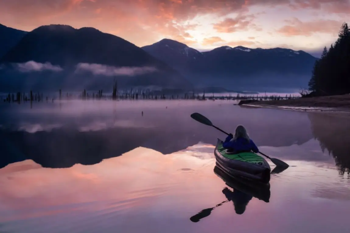 A woman paddling an inflatable kayak at sunset in the mountains