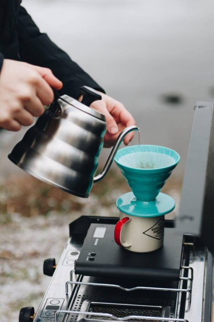 Someone pouring water into a blue pourover coffee set up from one of the best camp percolator models on a camp stove