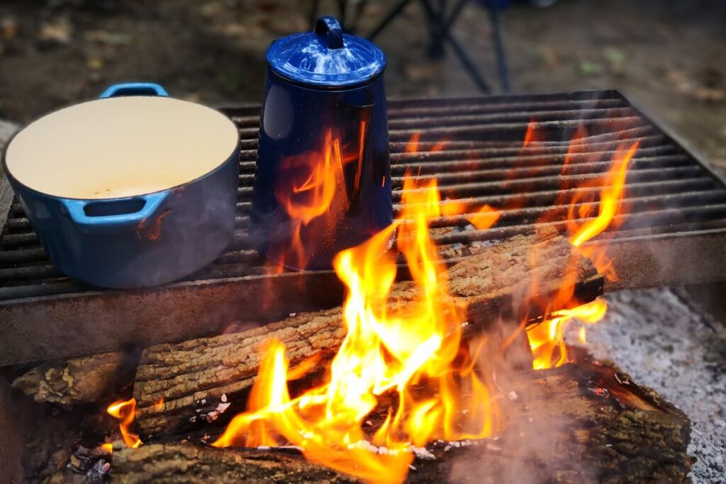 A blue camping percolator and pot on a grate over a campfire