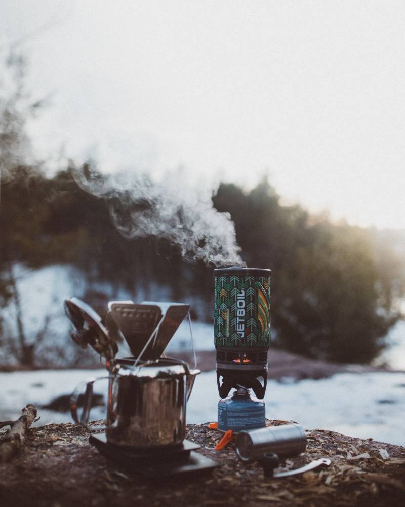 A JetBoil stove with steam coming from it next to a pourover set up over a camping percolator