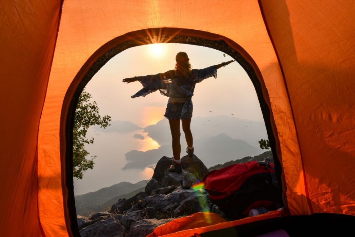 A photo taken through an orange tent of a women standing on a rock overlooking a mountain lake