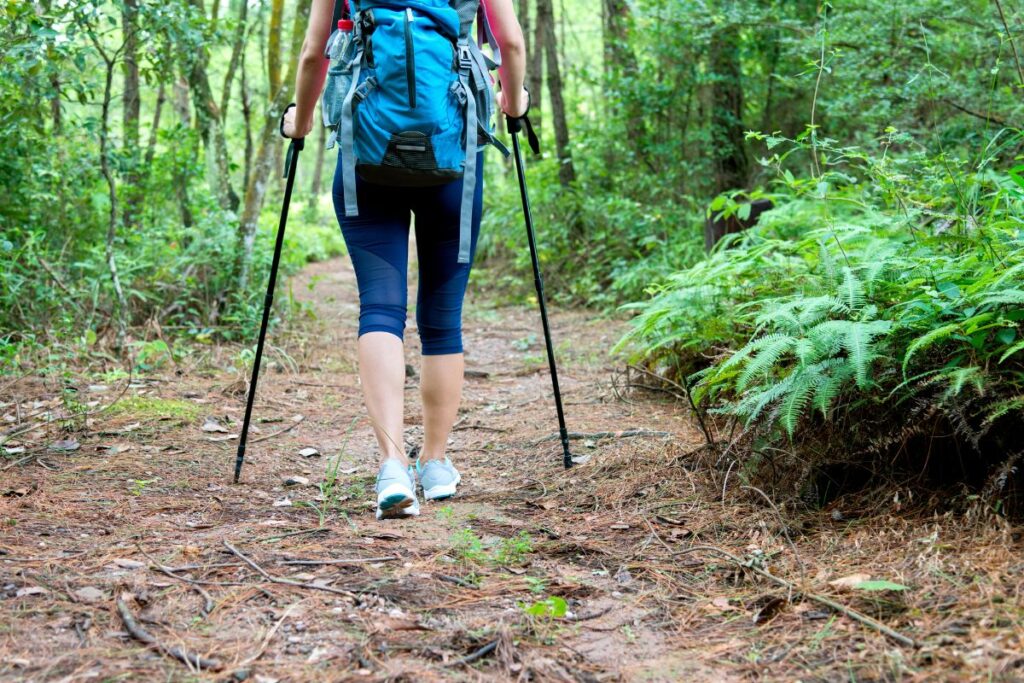 A woman hiking with a hiking backpack and trekking poles, one of the best outdoorsy gifts for her