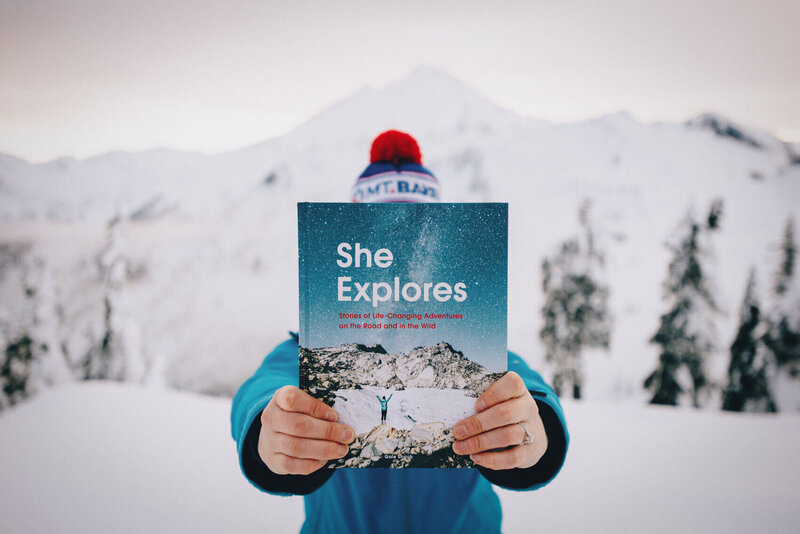A woman wearing a beanie and holding the She Explores book, one of the best outdoorsy gifts for women