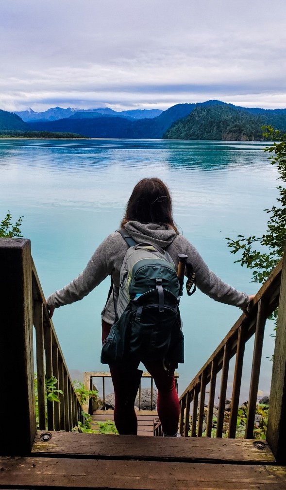 A woman wearing a hiking backpack and looking out over the water in Alaska