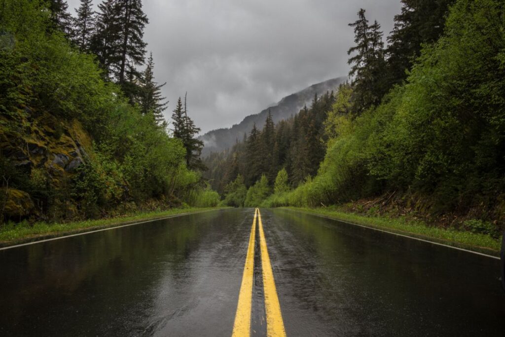 A wet highway, bright green forest, and mountains on a cloudy day along Alaska's Seward Highway