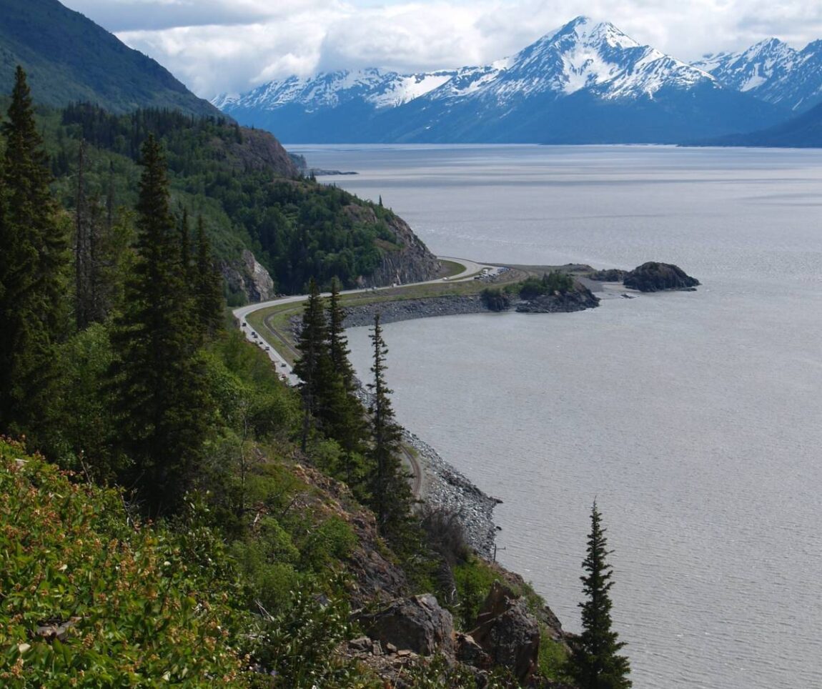 A curvy section of the Seward Highway along the Turnagain Arm from Anchorage to Seward, with snowy mountains in the distance