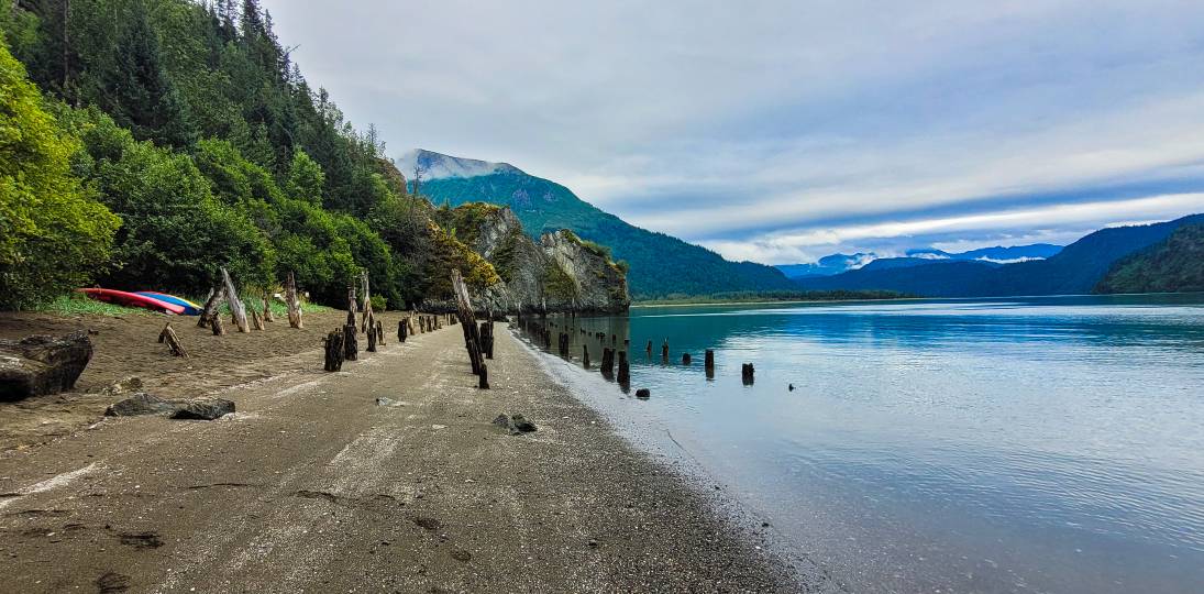 A beach with pilings and kayaks, surrounded by mountains in Halibut Cove near Homer Alaska