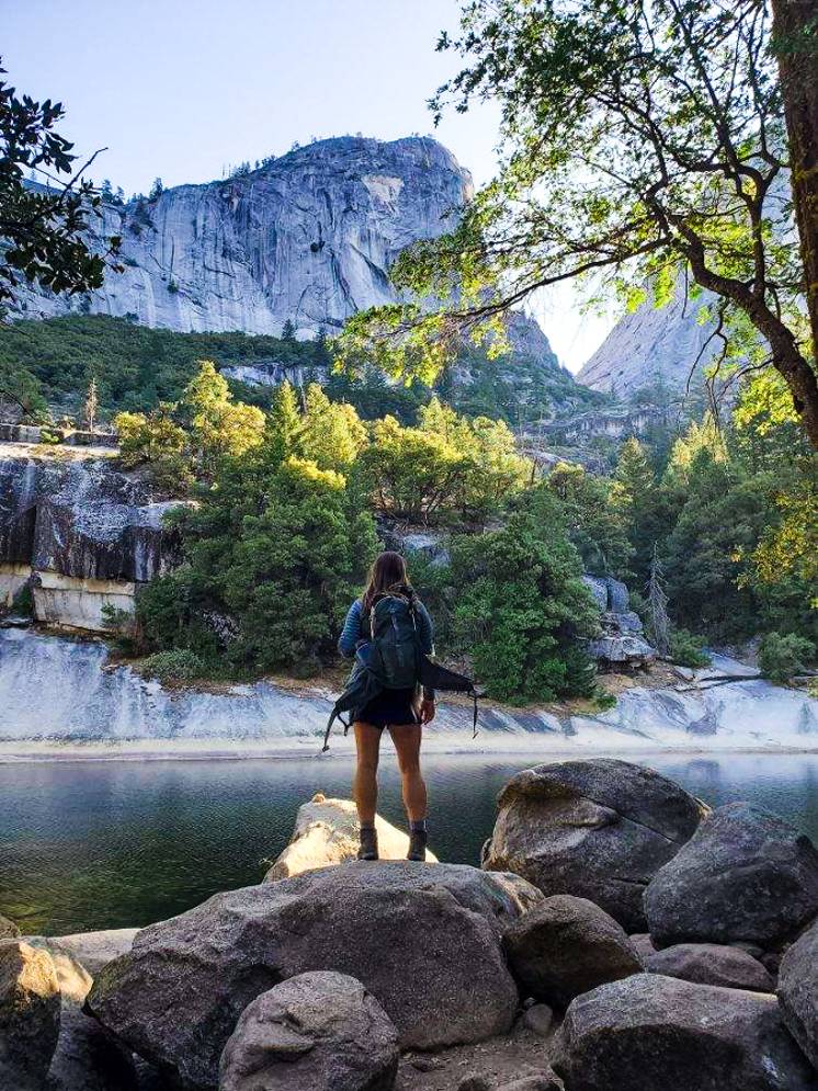 A woman who won the Half Dome lottery looking up at a mountain standing next to a lake