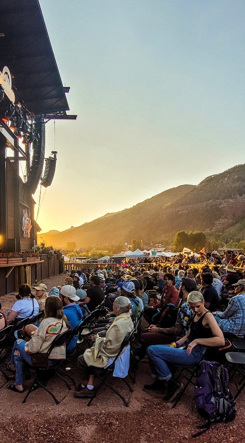 A crowd of people sitting in front of a stage at sunset during the 2022 Telluride Bluegrass Festival