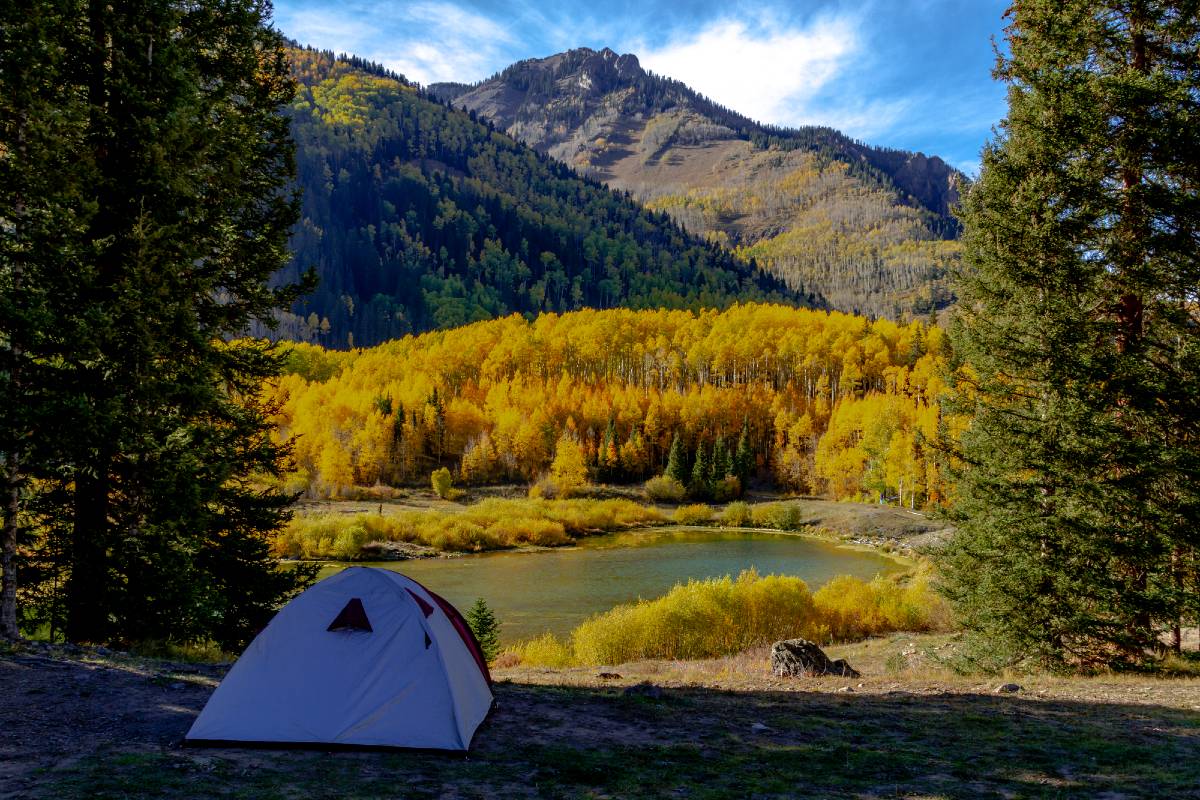A white tent pitched overlooking a small lake near mountains during fall, one of the best times for Telluride camping