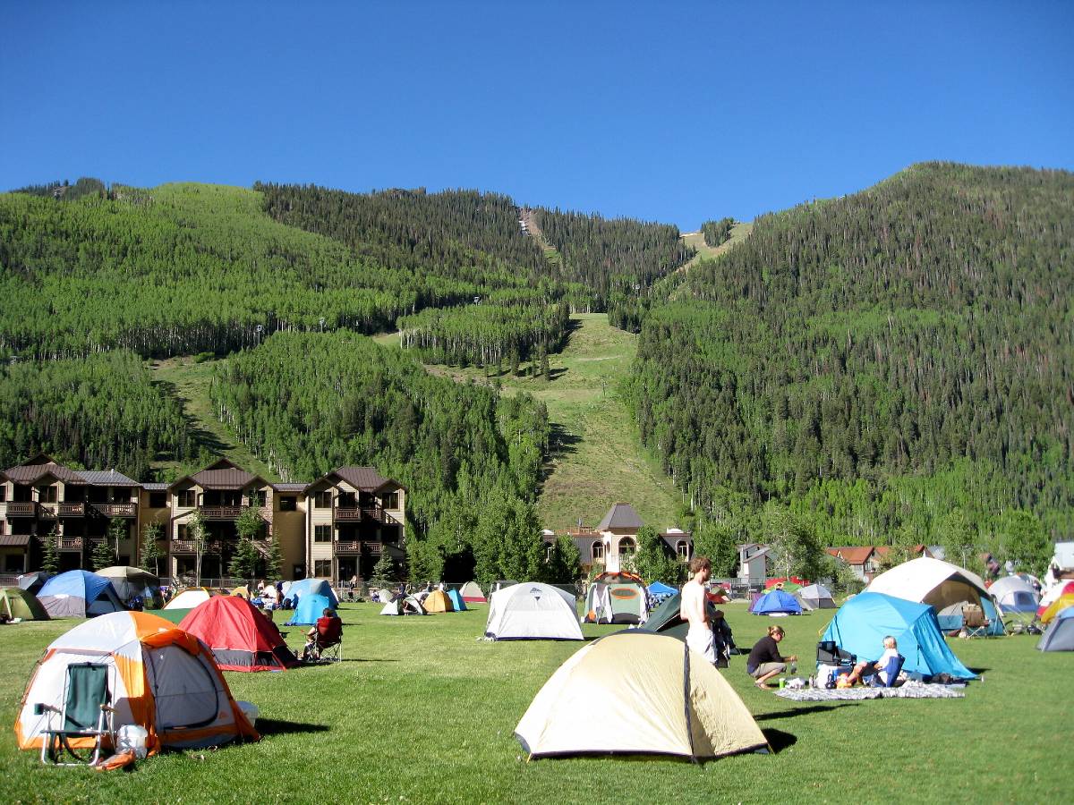 Many colorful tents set up on a green field in Town Park Campground, one of the best campsites near Telluride, near condos and ski runs 