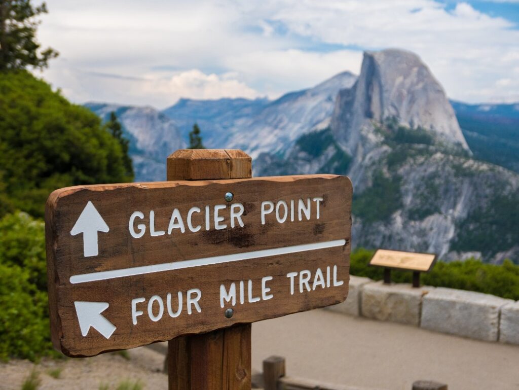 A trail sign pointing to Four Mile Trail and Glacier Point, one of the best short hikes in Yosemite, with Half Dome in the background