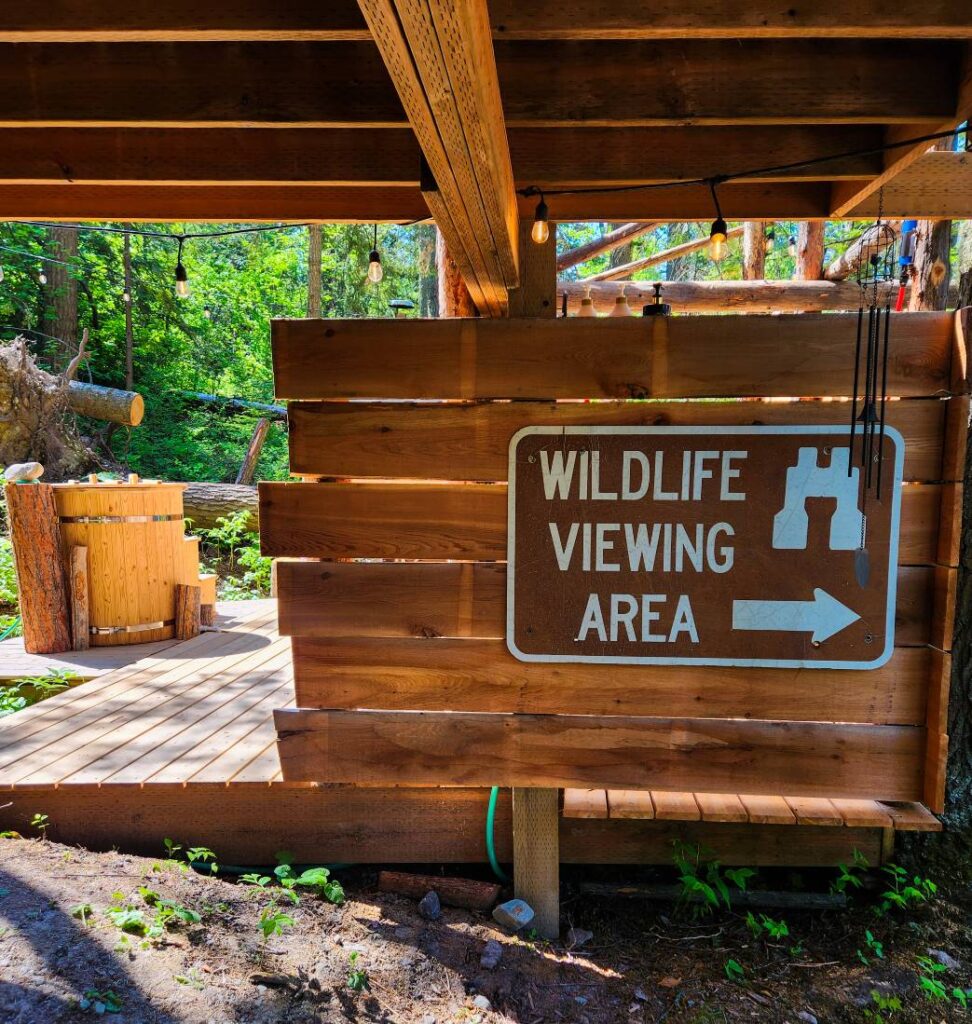 A sign that says Wildlife Viewing Area on a fence, with a cold plunge in the background at a wall tent where you can go glamping in Montana