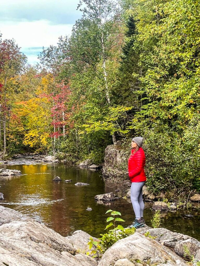 A woman standing on a rock overlooking a river and wearing leggings and a puffy jacket, some of the best hiking tips for beginners