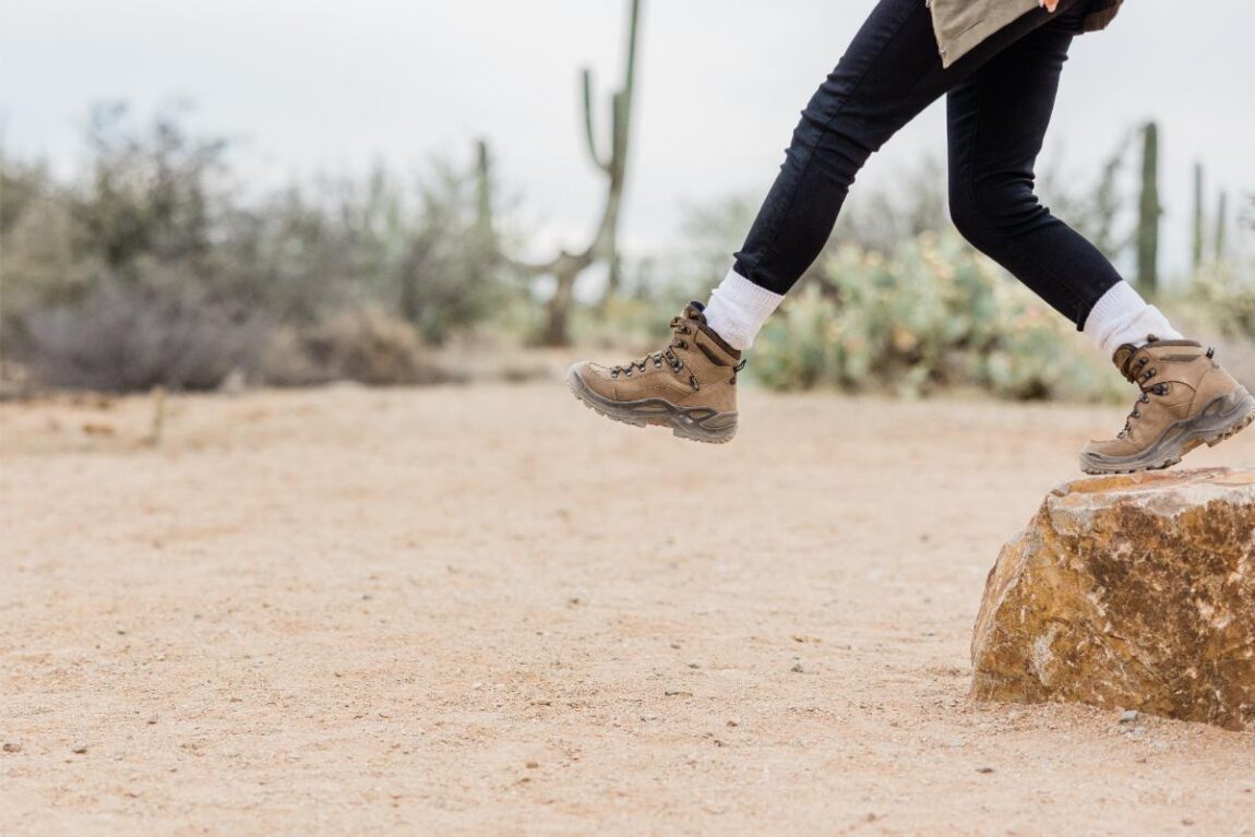 A woman wearing hiking leggings and boots in the desert, stepping off a rock