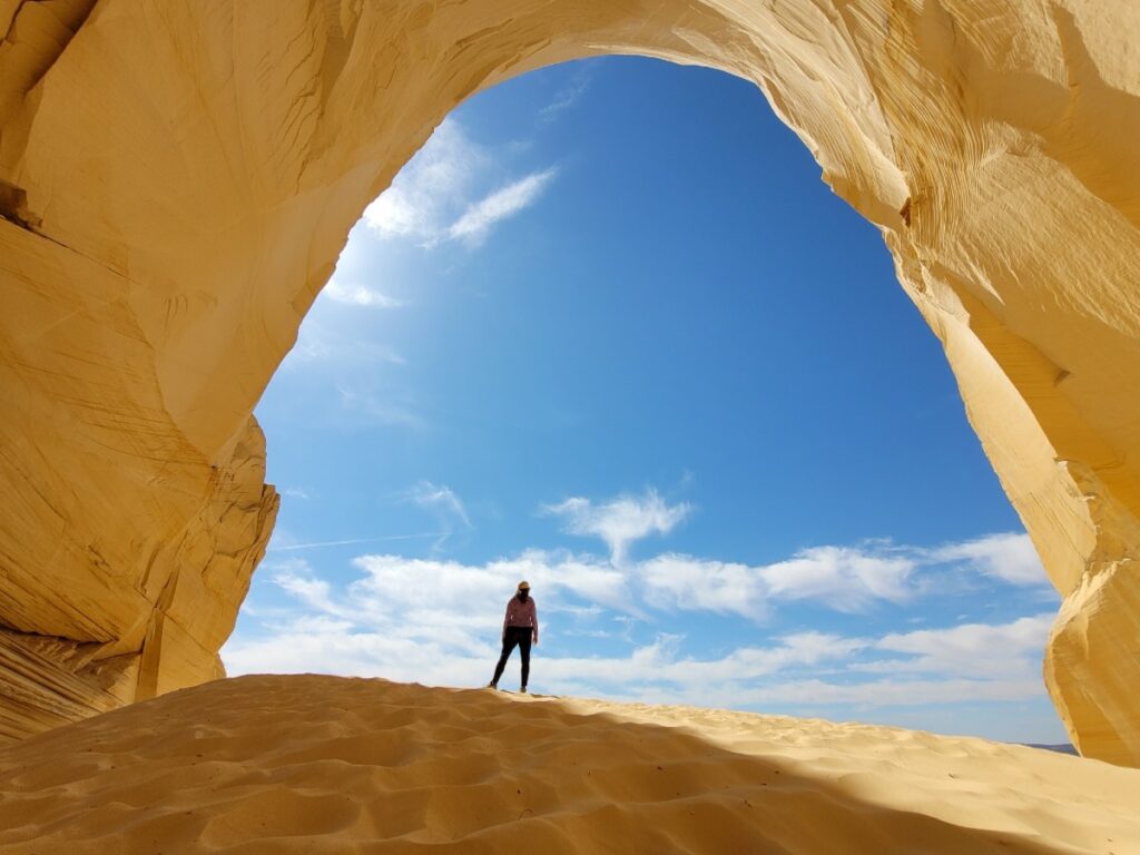 A woman standing on top of a sand dune in the archway at the Great Chamber in Utah