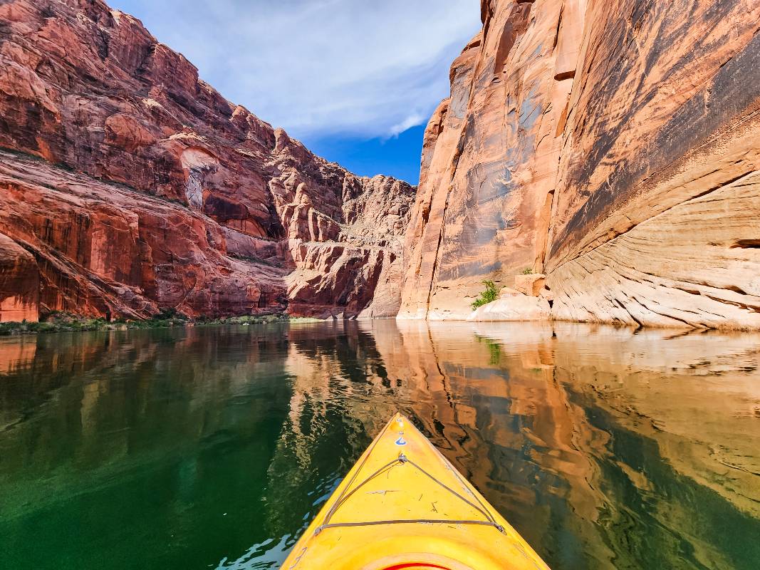 The front of a yellow kayak heading toward a canyon while kayaking Horseshoe Bend