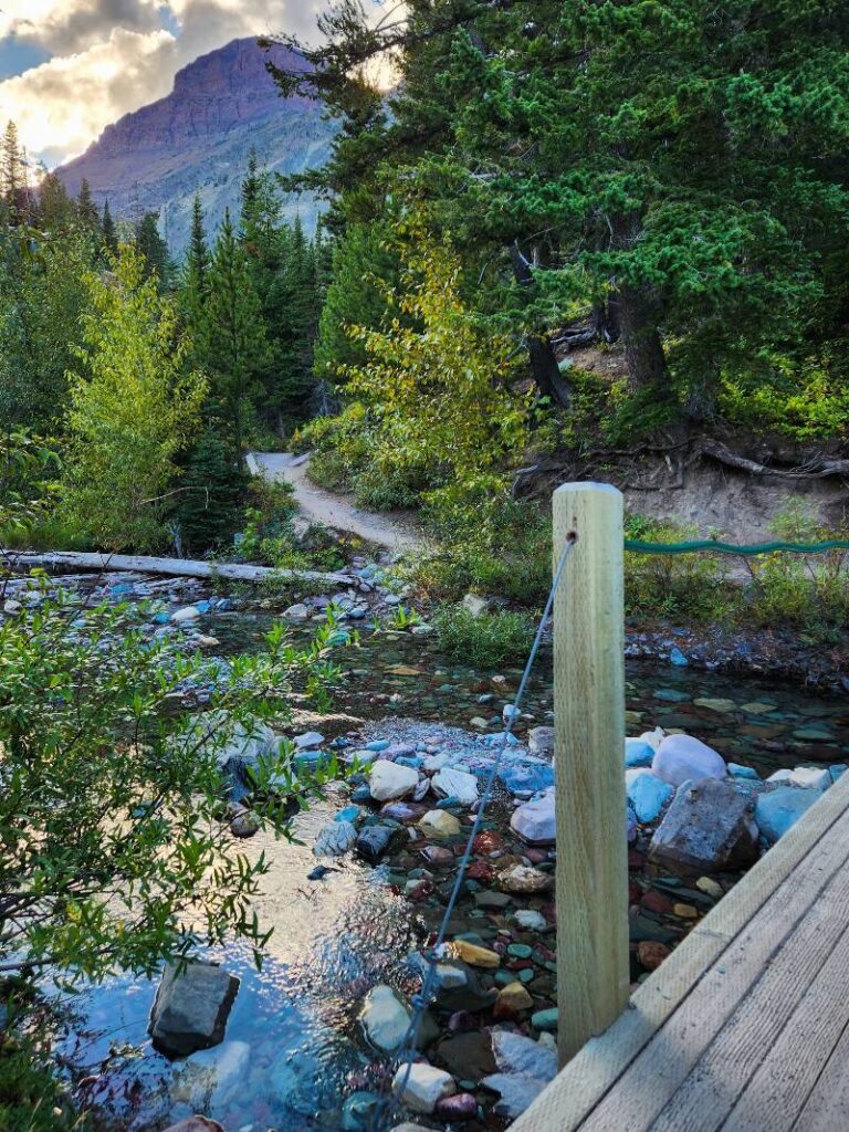 A bridge over a creek and a portion of dirt trail leading to Running Eagle Falls Glacier National Park