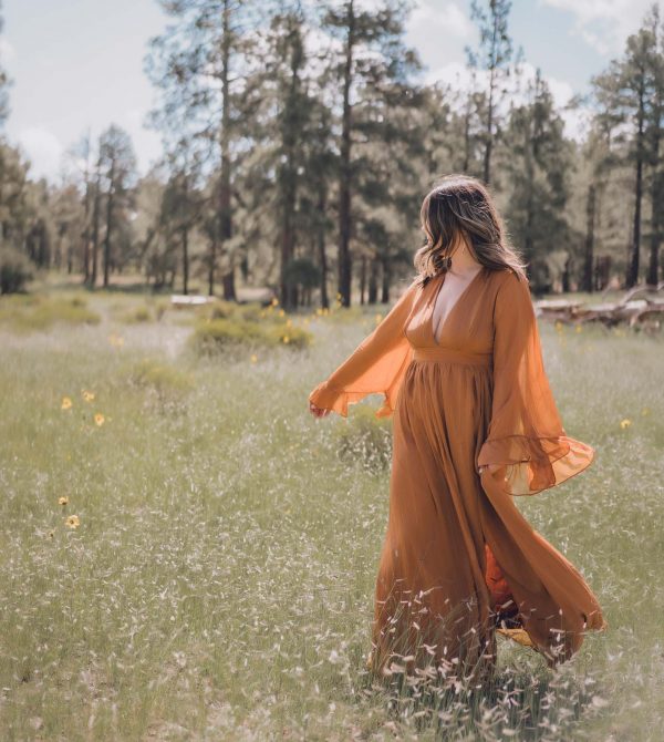 Taryn Shorr, a freelance travel writer, walking through an open field in a forest wearing an orange dress