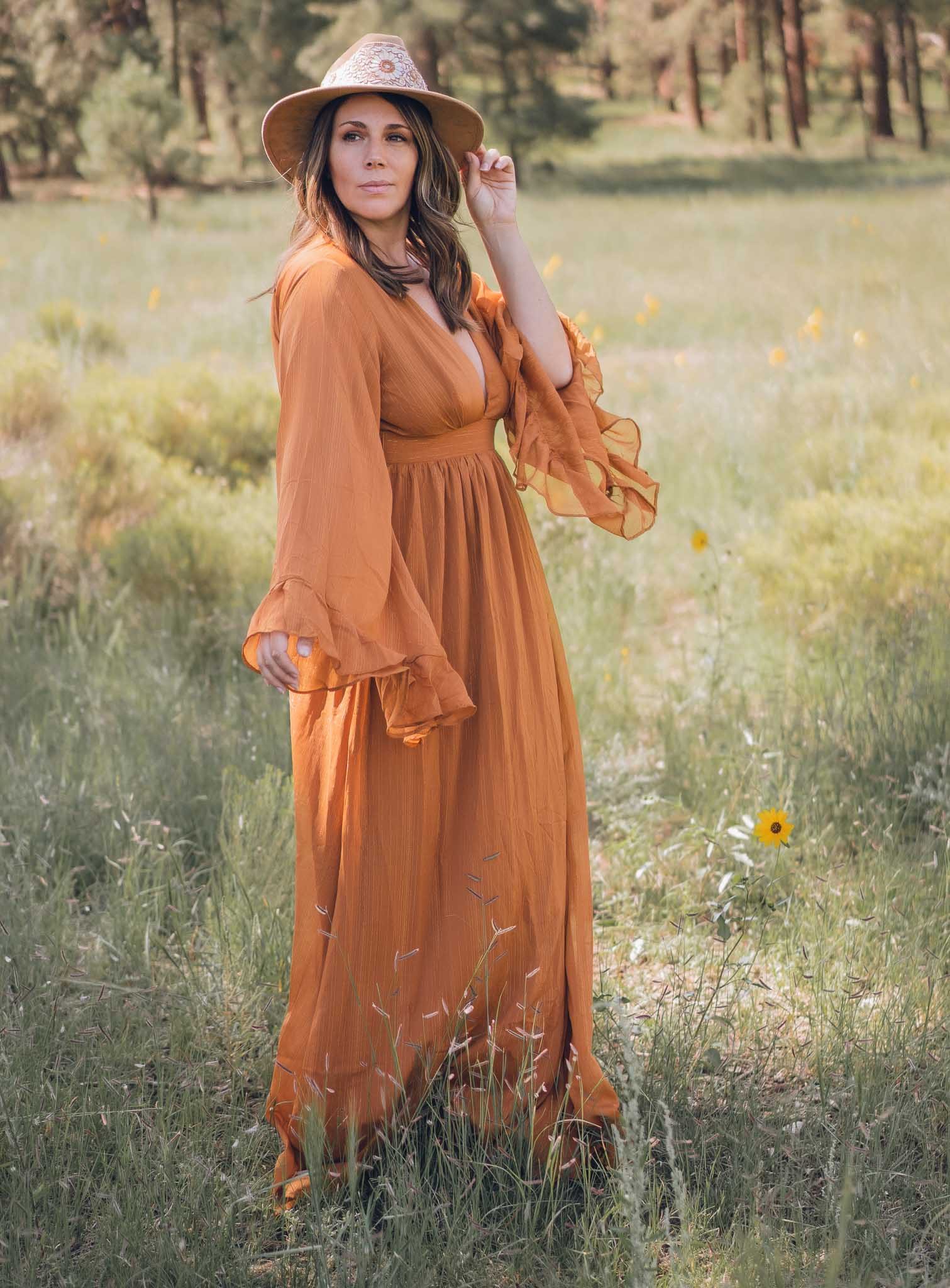 Taryn Shorr, a freelance travel writer, wearing an orange dress and a hat in a field